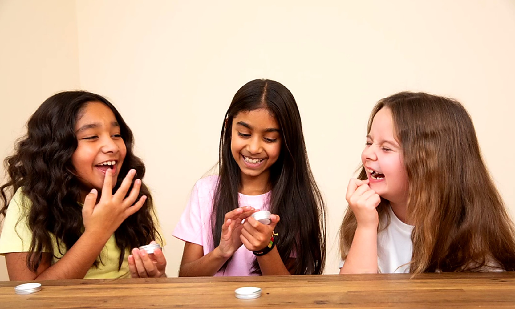 Three children laughing as they try Yani Beauty flavoured lip balm tins at a party table